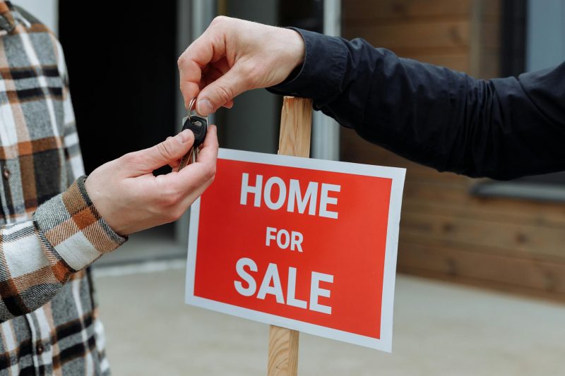 Closeup of a home for sale sign with people exchanging keys