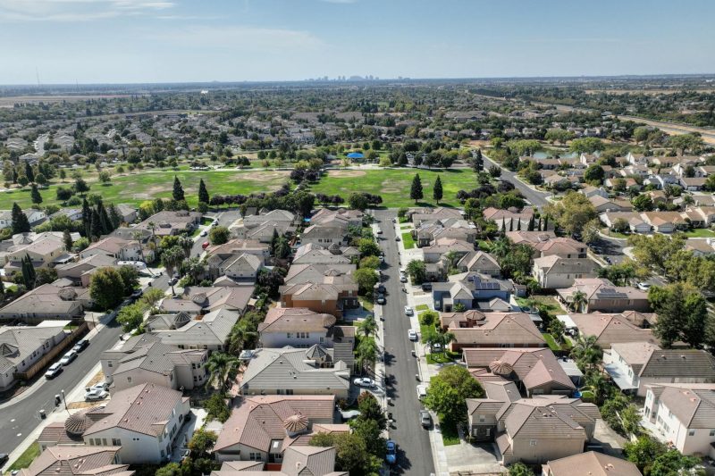 Aerial view of a Sacramento suburb featuring rows of houses surrounded by lush greenery on a sunny day.