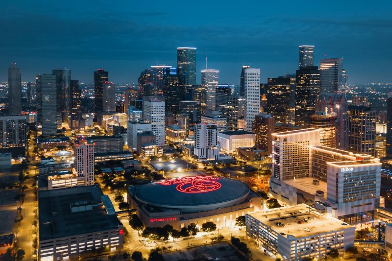 Aerial view of Houston's illuminated skyline at night, featuring modern skyscrapers glowing against the dark sky.