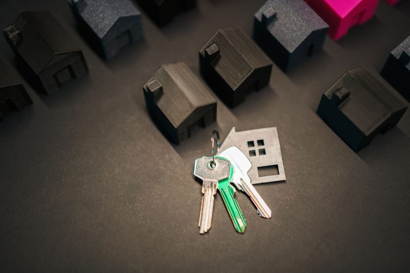 Miniature house models alongside an assortment of colorful keys on a textured surface.
