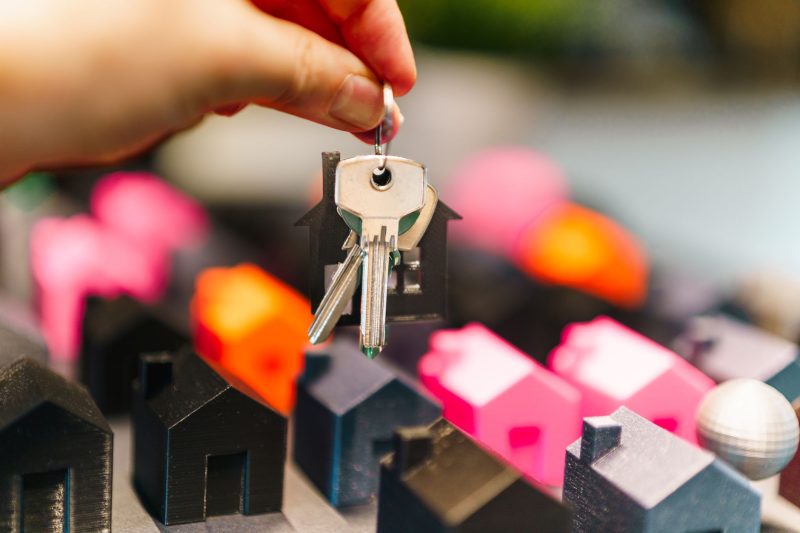 Colorful miniature houses arranged with a hand holding a set of keys.